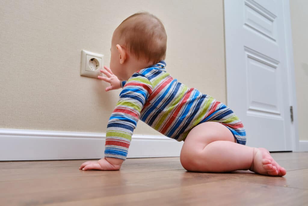 Baby toddler reaches into the electrical outlet on the home wall with his hand. Danger and protection of child fingers from electric shock