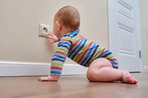 Baby toddler reaches into the electrical outlet on the home wall with his hand. Danger and protection of child fingers from electric shock